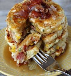 stack of pancakes with bacon and cheese on yellow plate next to fork, closeup