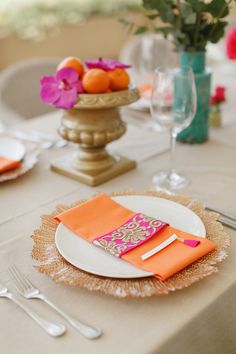 the table is set with orange napkins, silverware and flowers in vases