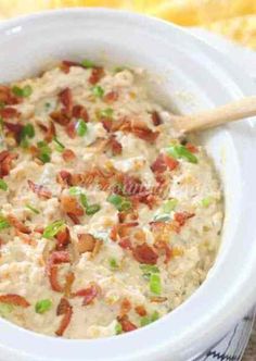 a close up of a bowl of food with bacon and green onions in it on a table