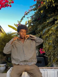 a young man sitting on top of a white bench next to a bush and flowers