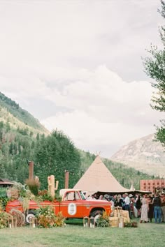 an old red truck parked in front of a teepee tent with people standing around it