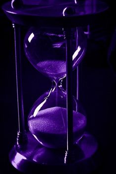 an hourglass sitting on top of a table with purple light in the dark behind it