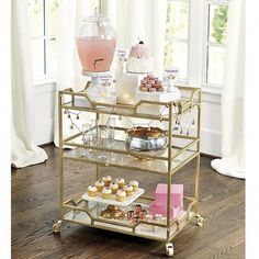 a gold serving cart filled with cupcakes and pastries on top of a hard wood floor