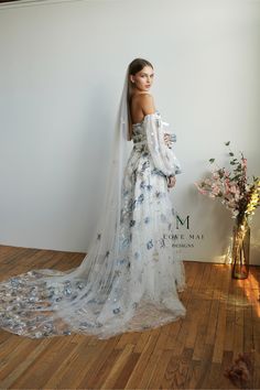 a woman in a wedding dress standing next to a vase with flowers on the floor