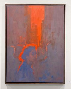 a painting hanging on the wall in front of a woman's face with an orange light behind her