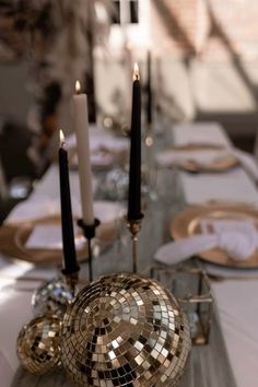 a table topped with lots of candles and plates covered in disco ball mosaics on top of a wooden table