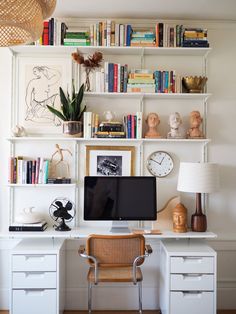 a desk with a computer on top of it next to a book shelf filled with books