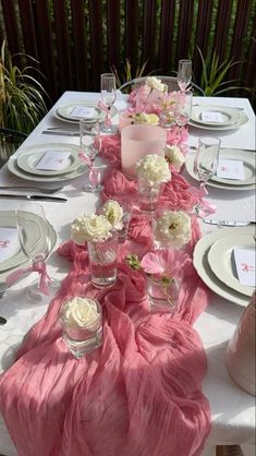 a long table is set with pink and white flowers, silverware, and napkins