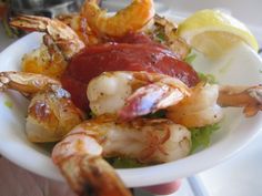 a white bowl filled with shrimp and sauce on top of a table next to lemon wedges