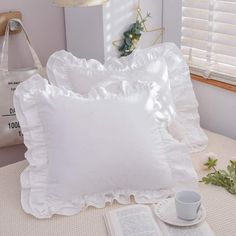 two white pillows sitting on top of a bed next to an open book and cup