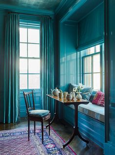 a room with blue walls and curtains, a table with two teapots on it