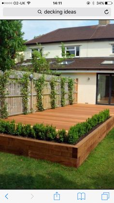 a wooden deck surrounded by plants in front of a house