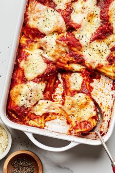 a casserole dish with meat and cheese on it, next to two bowls of seasonings