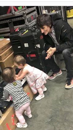 a woman kneeling down next to two small children in front of boxes and other items