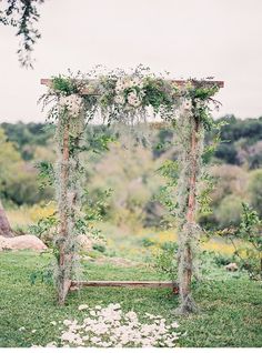 an outdoor wedding ceremony setup with greenery and flowers on the arbor, surrounded by lush green grass