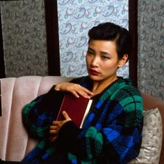 a woman is sitting on a couch with a book in her hand and looking at the camera