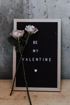 two roses sitting on top of a wooden table next to a sign that says be my valentine