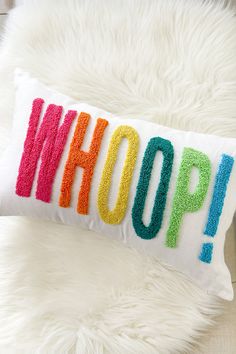 a pillow with the word whoop on it sitting on a white fur rug next to a stuffed animal