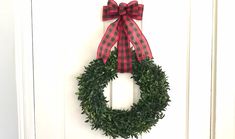 a wreath hanging on the front door of a house with red and black plaid ribbon