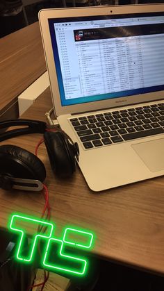 an open laptop computer sitting on top of a wooden desk next to headphones and a mouse