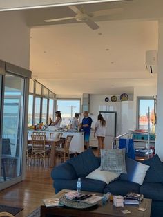 people are standing in the living room looking out at the ocean from the kitchen and dining area