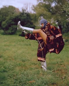 a woman in an animal print coat and hat is dancing on the grass with her legs spread out