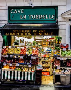 a fruit and vegetable stand in front of a building with french writing on the sign