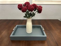 a white vase filled with red flowers on top of a wooden table