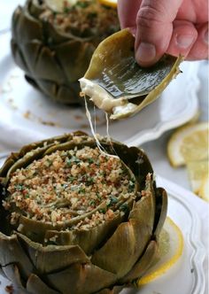 someone is dipping something into an artichoke on a plate with lemon wedges