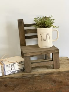 a wooden chair with a coffee mug on top of it next to books and a plant