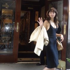 a woman in a black dress is walking out of a building with her hand up