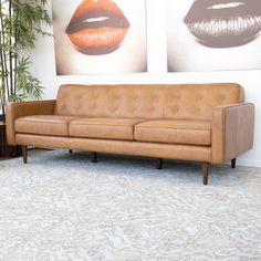 a tan leather couch sitting in front of two pictures on the wall with orange lips