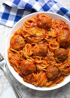 a bowl filled with spaghetti and meatballs on top of a blue checkered table cloth