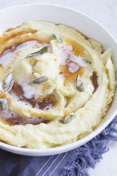 a white bowl filled with mashed potatoes covered in sauce and sage sprinkles