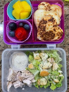 a plastic container filled with food next to fruit and salad on top of a table