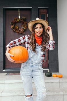 a woman wearing overalls and a hat holding a pumpkin