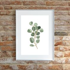 a white frame hanging on a brick wall next to a green leafy plant print