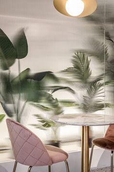 two pink chairs sitting at a round table in front of a wall with palm leaves on it