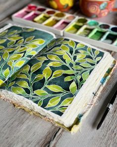 an open book sitting on top of a wooden table next to paintbrushes and paints