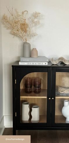 a black cabinet with glass doors and vases on the top shelf next to it