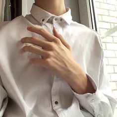 a man wearing a white shirt is holding his hand on his chest and looking out the window