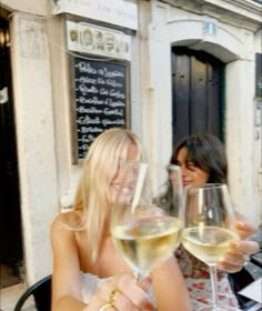 two women sitting at an outdoor table with wine glasses