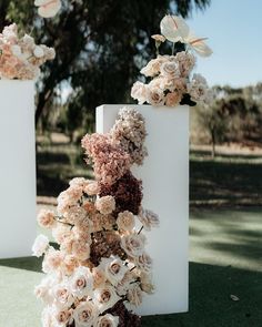 two tall white vases with flowers on them sitting in the grass next to each other