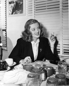 a black and white photo of a woman sitting at a table with food in front of her