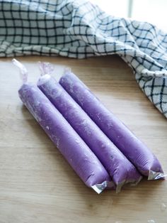 three purple candles sitting on top of a wooden table next to a cloth covered bag