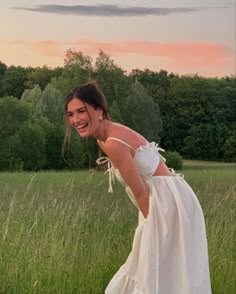 a woman in a white dress walking through tall grass