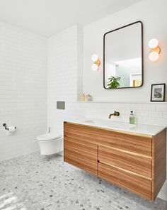 a bathroom with white tile and wooden cabinetry in the center, along with a large mirror on the wall