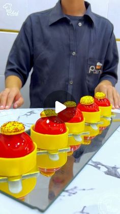 a man standing in front of a table filled with small yellow and red cakes on top of