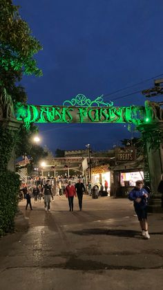 people walking under a green sign that says forest park on it's side at night