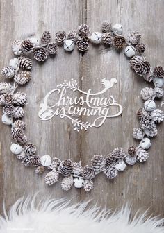 a christmas decoration made out of pine cones and white feathers on a wooden background with the words christmas evening written in cursive writing